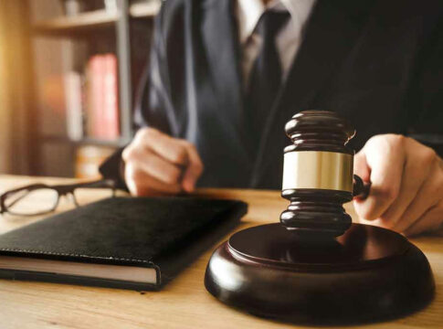Judges hand holding gavel near book and glasses.