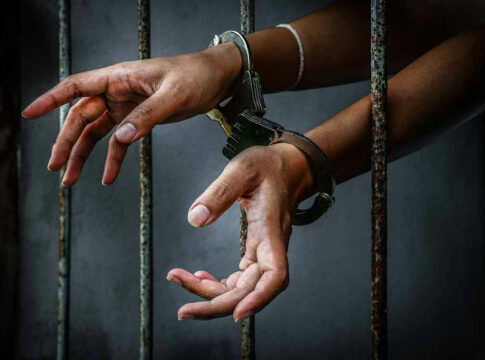 Handcuffed hands reaching through jail cell bars.