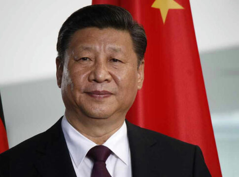 Man in suit standing before Chinese flag.