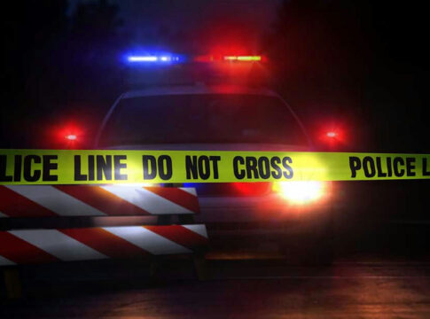 Police car behind yellow caution tape at night.