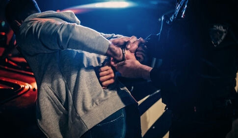 Person being handcuffed by an officer beside a police car at night